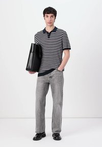 Striped polo shirt, navy and white, with a collar and three buttons; paired with light grey jeans and black shoes; holding a black bag.