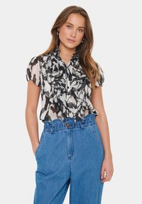 Black and white ruffled blouse with short sleeves and a buttoned front, worn with high-waisted blue denim trousers.