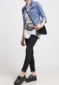 Jeansjacka med knappar och fickor, grafisk vit t-shirt, svarta skinny jeans och svarta texturerade sneakers med platåsula.