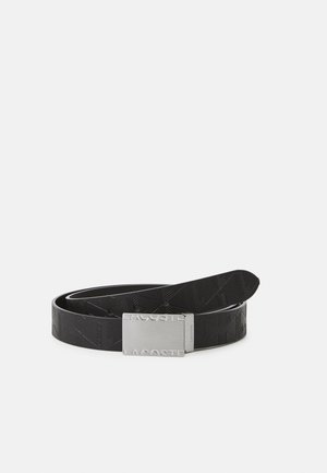 Black leather belt featuring embossed geometric patterns, finished with a rectangular silver buckle inscribed with "Lacoste."