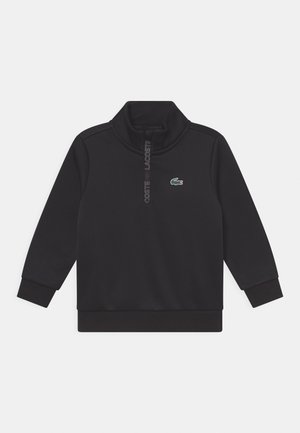 Schwarzer Pullover mit langen Ärmeln, Viertelreißverschluss, gerippten Bündchen und kleinem grün-weißem Krokodil-Logo auf der linken Brust.