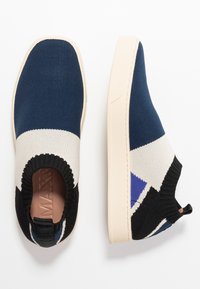 Slip-on sneakers med en stickad ovandel i marinblått, svart och vitt med geometriska mönster, kontrasterande sula och en texturerad yta.