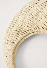 Woven straw bag in cream, curved shape, detailed with a braided texture. Smooth finish with tight weaves and minimalistic design.