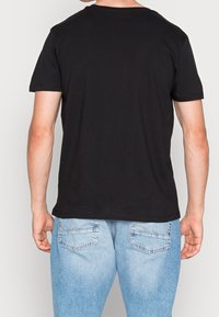 Černé tričko s krátkým rukávem a kulatým výstřihem, vyrobené z bavlny, s jednoduchým designem. Nosené s světle modrými džíny.