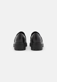 Scarpe in pelle nera con una finitura liscia, punta rotonda e suola in gomma spessa e strutturata. Design minimalista senza marchi o accenti visibili.