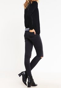 Svart långärmad topp med texturerad rygg, kombinerad med svarta skinny jeans med slitna knän och klackiga ankelstövlar.