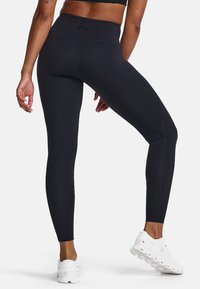 Schwarze hoch taillierte Leggings aus dehnbarem Material mit schlankem Design, ausgestattet mit flachen Nähten und eng anliegender Passform, kombiniert mit weißen Sportschuhen.