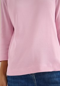 Lyserød ribbet bluse med lange ærmer og rund halsudskæring, med en lige kant og tætsiddende ærmer, kombineret med mørkeblå denimjeans.