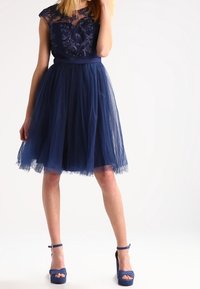 Námořnická modrá šaty s průhledným vyšívaným korzetem, tylovou sukní a přiléhavým pasem. Doplněné o odpovídající modré lodičky na vysokém podpatku.