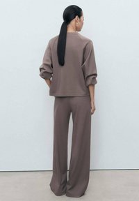 Hnědý dvoudílný outfit skládající se z volného topu s nabíranými rukávy a kalhot s širokými nohavicemi. Měkká textura, minimalistický design, žádné viditelné vzory.