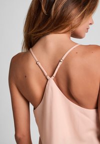 Licht perzikkleurige mouwloze top met dunne verstelbare bandjes, voorzien van een gladde textuur en een lage ruguitsnijding die het schouderbladgebied accentueert.