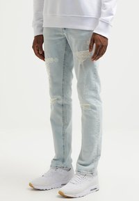 Light blue distressed jeans worn with white sneakers and a white long-sleeve top, visible from waist down to feet.