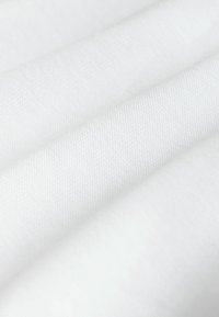 Biała tkanina o teksturowanej powierzchni, z zagiętymi warstwami, które tworzą głębię i subtelne cienie. Materiał wydaje się gładki i jednolity.