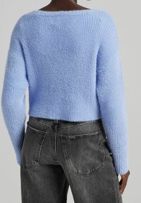Světlomodrý, nadýchaný pletený svetr s širokým výstřihem a dlouhými rukávy, v kombinaci s tmavě šedými džíny s vysokým pasem a zadními kapsami.