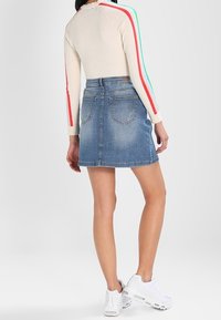 Crèmefärgad långärmad topp med röda och gröna ränder. Högmidjad jeanskjol i blått med två bakfickor och rak skärning. Vita sneakers.