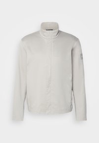Lys grå, langermet jakke med høy krage, glatt tekstur, frontlukking og subtil merkevare på ermet. Minimalistisk design.