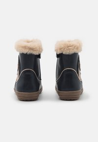 Botas de tobillo azul oscuro con un suave collar beige, cremalleras laterales y una suela texturizada en tono marrón, con un acabado de cuero liso.