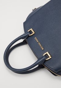 Granatowa torebka skórzana teksturowana z podwójnymi uchwytami, złotym zamkiem błyskawicznym oraz złotym logo Michael Kors w górnej części.