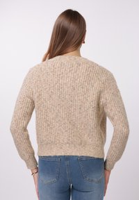 Suéter beige de punto con textura acanalada, longitud corta y mangas largas. Diseño casual con cuello redondo y material suave.