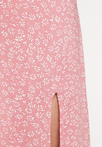 Rosa blommönstrad tyg med små vita blommor, som har en sidoklyvning för detalj och en mjuk, texturerad yta.
