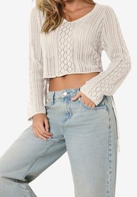 Virkat, krämfärgat crop top med V-ringning och lång ärm; kombinerat med ljusblå högmidjade jeans med avslappnad passform.