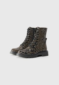 Bottes de combat à imprimé serpent marron et noir avec un laçage à l'avant, une fermeture éclair et une semelle robuste. Tige texturée avec un léger éclat.