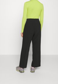 Svarta vida byxor med en slät textur, tillsammans med en långärmad, ribbad limegrön topp och grå sportskor med neondekorationer.