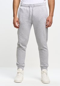 Grå bomulds sweatpants med elastisk talje og hvid snor, der har sidelommer og ribbede manchetter, båret med hvide sneakers.