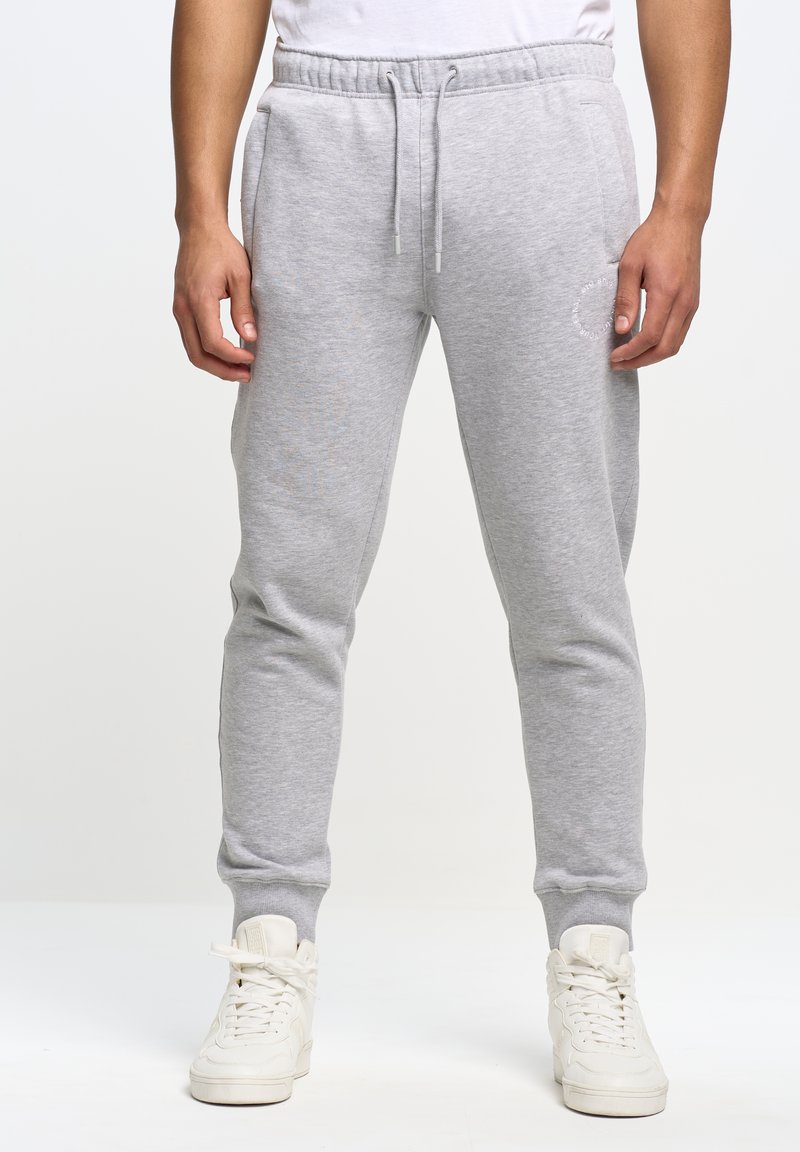 Grå bomulds sweatpants med elastisk talje og hvid snor, der har sidelommer og ribbede manchetter, båret med hvide sneakers.