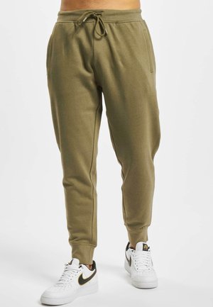 Olive green sweatpants with a drawstring waist, tapered legs, side pockets, and ribbed cuffs, worn with white sneakers featuring black accents.