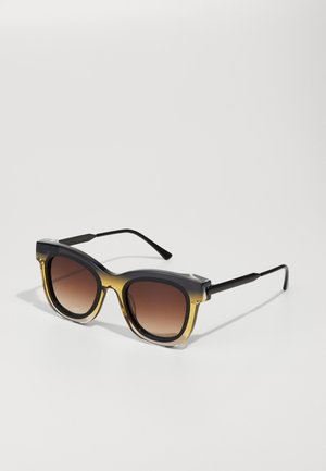 Lunettes de soleil avec une monture dégradée orange à noir, des verres carrés surdimensionnés et des branches noires, présentant une finition brillante.