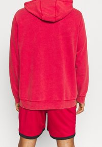 Sweat-shirt rouge à capuche, avec poignets et ourlet côtelés. Accompagné d'un short rouge avec bordure noire, mettant en avant un tissu léger et un design sportif.
