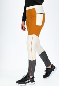 Kleurgeblokte leggings in oranje, wit en grijs. Gemaakt van rekbaar materiaal met contrasterende naden en zakken. Gecombineerd met zwarte sneakers.