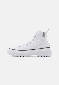White high-top sneakers with canvas material, a textured sole, lace-up front, side zipper, and a black rubber accent along the sole.