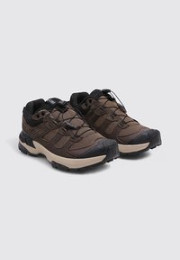 Chaussures de randonnée marron en mesh et daim avec des accents noirs, dotées d'une semelle texturée, de lacets élastiques et d'un col rembourré pour le confort.