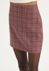 Gonna a scacchi rossi con un design aderente, tessuto testurizzato e orlo poco sopra la metà della coscia. Presenta un sottile motivo a griglia bianca.