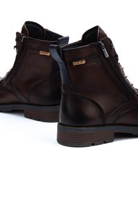 Bottines en cuir marron avec bout rond et talon empilé. Comprend une fermeture éclair sur le côté, des lacets contrastés et des détails du logo de la marque.