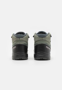 Zapatillas de senderismo en verde y negro con un diseño de caña alta, tejido texturizado, talón reforzado y suela de goma preparada para senderos.