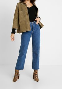 Oliwkowa, oversize'owa kurtka, czarny sweter z prążkowanym wzorem, niebieskie jeansy o podwyższonym stanie oraz buty na obcasie w wzór wężowej skóry z blokowym obcasem.