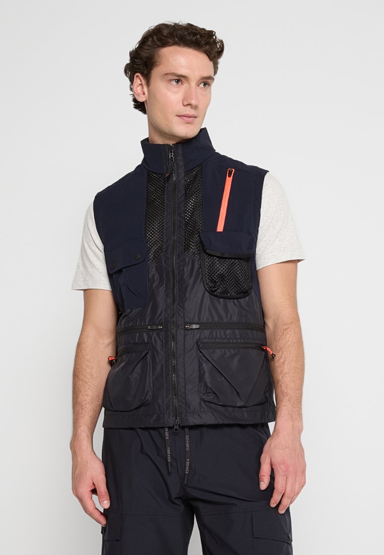 Marinefarbene Weste mit Reißverschluss vorne, Netzpaneel, mehreren Taschen und einem kontrastierenden orangen Reißverschluss. Mit einem leichten, strukturierten Stoffdesign.
