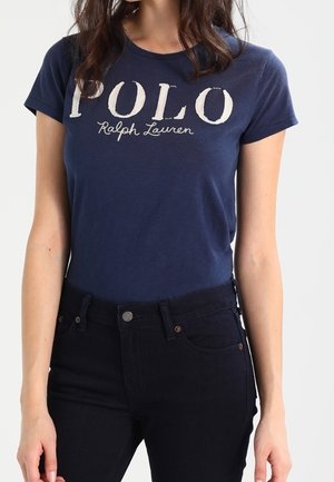 T-shirt en coton bleu marine avec logo blanc "POLO Ralph Lauren", à manches courtes et coupe classique. Porté avec un jean en denim foncé.