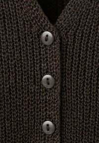 Tissu tricoté marron foncé avec trois boutons gris brillants attachés en ligne verticale sur un vêtement.