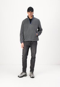 Gray fleece pullover with a half-zip neck and blue accents, paired with dark jeans and gray hiking shoes, model wearing a black hat.