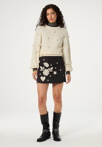 Crème wolken trui met bloempompons; zwarte mini-jurk met geborduurde bloemen, sterren en harten; gecombineerd met kniehoge zwarte laarzen.