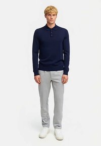 Mörkblå tröja med långa ärmar, krage och knappar, kombinerad med ljusgråa mjukisbyxor och vita sneakers. Mjuk textur genomgående.