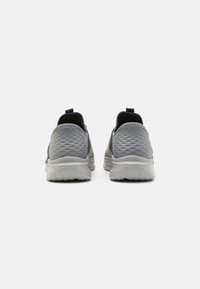 Chaussures de sport grises avec une tige texturée, des accents noirs, une semelle rembourrée et une languette à l'arrière pour un enfilage facile.