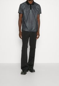 Černé polokošile s geometrickými vzory, krátké rukávy a límec, spárované s černými kalhotami ve stylu cargo a černými teniskami.