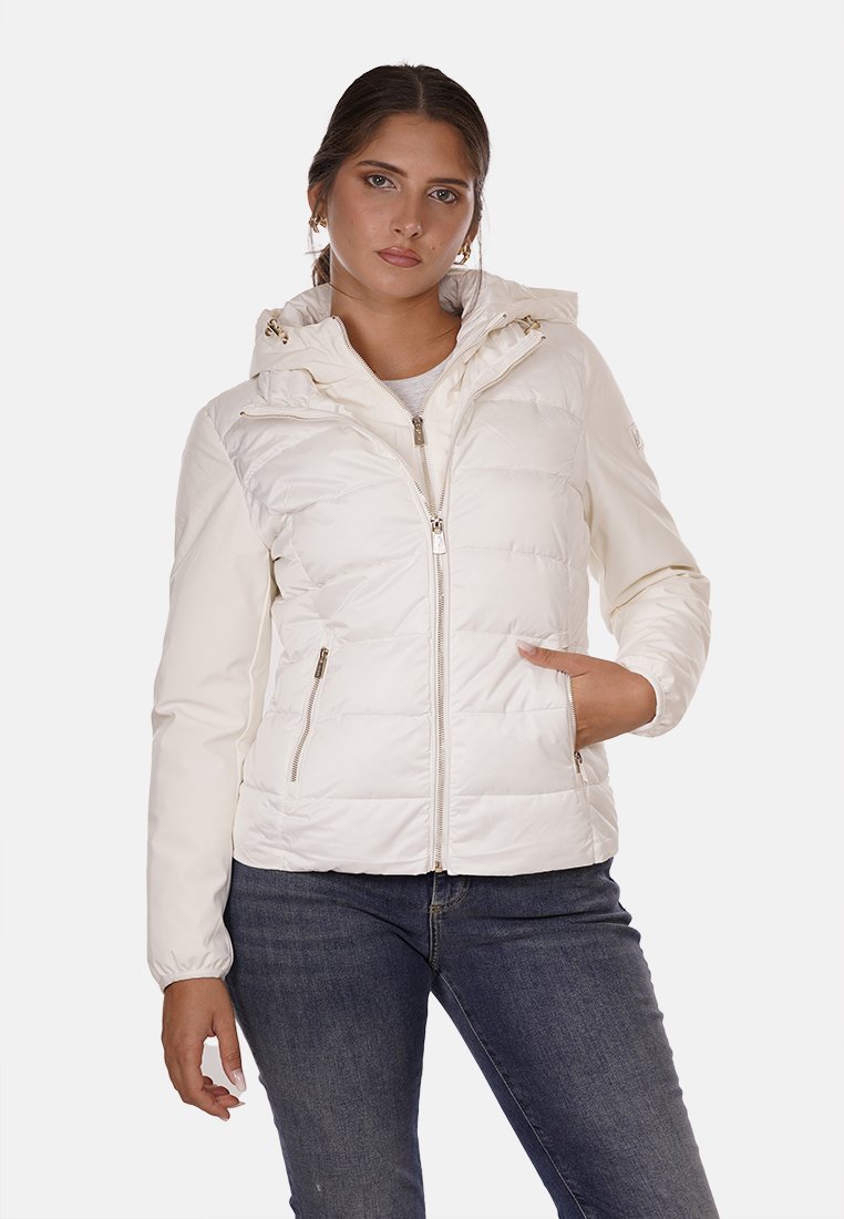 Giacca puffer bianca leggera con cappuccio, chiusura con zip, tasche laterali e texture trapuntata, indossata sopra una maglietta grigia e jeans blu.