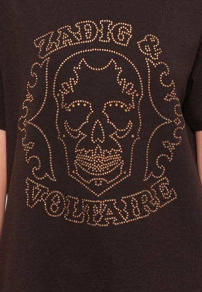 Čierne bavlnené tričko s dizajnom lebky pokrytej zlatými korálkami a ornamentálnymi akcentmi, pod grafikou je text "ZADIG & VOLTAIRE".