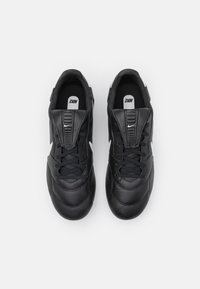 Scarpe da ginnastica in pelle nera con superficie testurizzata, dotate di un design con lacci e accenti di branding bianchi sui lati.